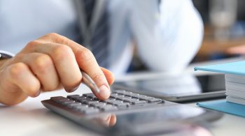 Hand of male businessperson making investment and income data calculations at office worktable close-up